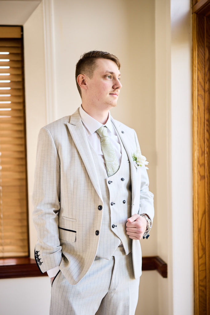 Groom in a cream three-piece suit looking out of a window