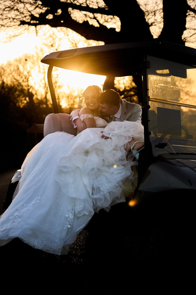 Bride and groom cuddled up in a golf buggy at sunset at Stock Brook Manor
