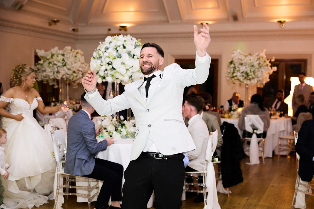 Man in a white jacket dancing between the tables with his arm in the air
