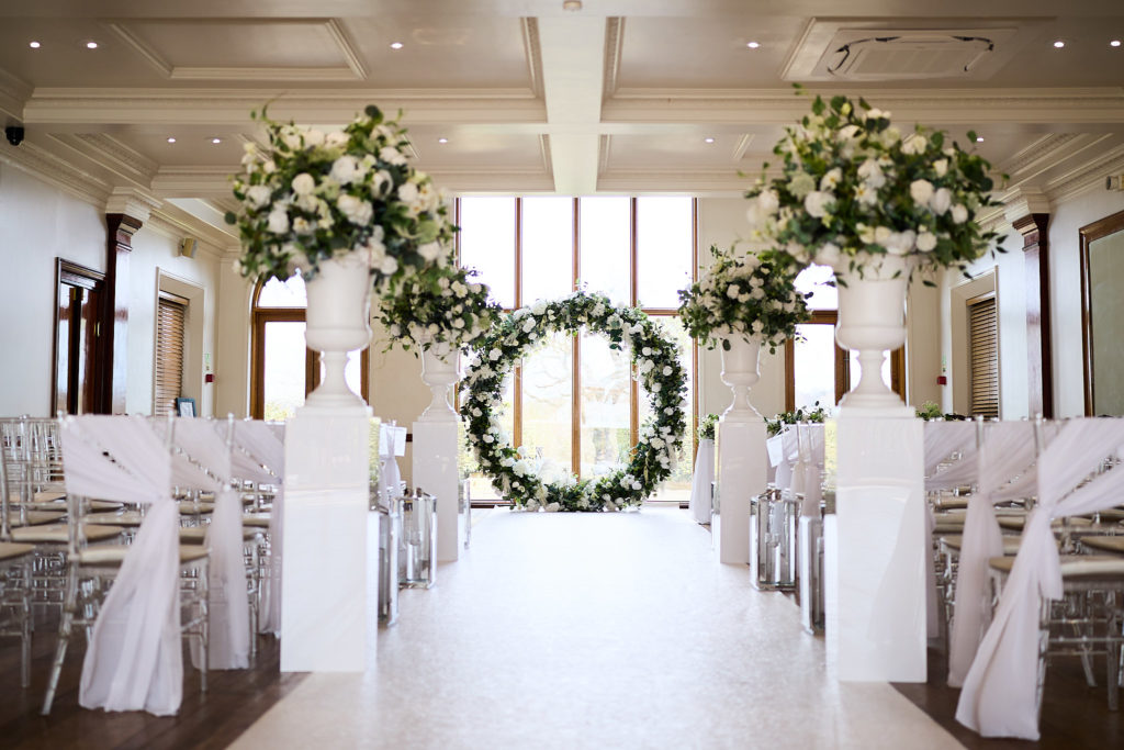 Ceremony room set with white chairs, urns of flowers and a circular floral arch