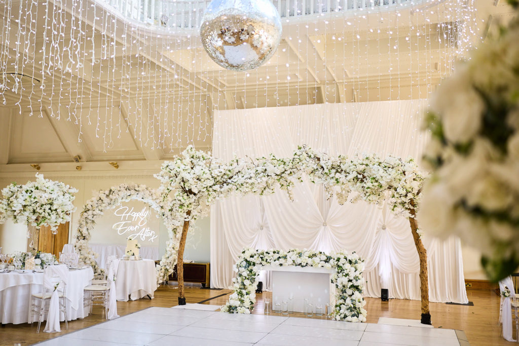 White dance floor with a floral arch under a ceiling of fairy lights
