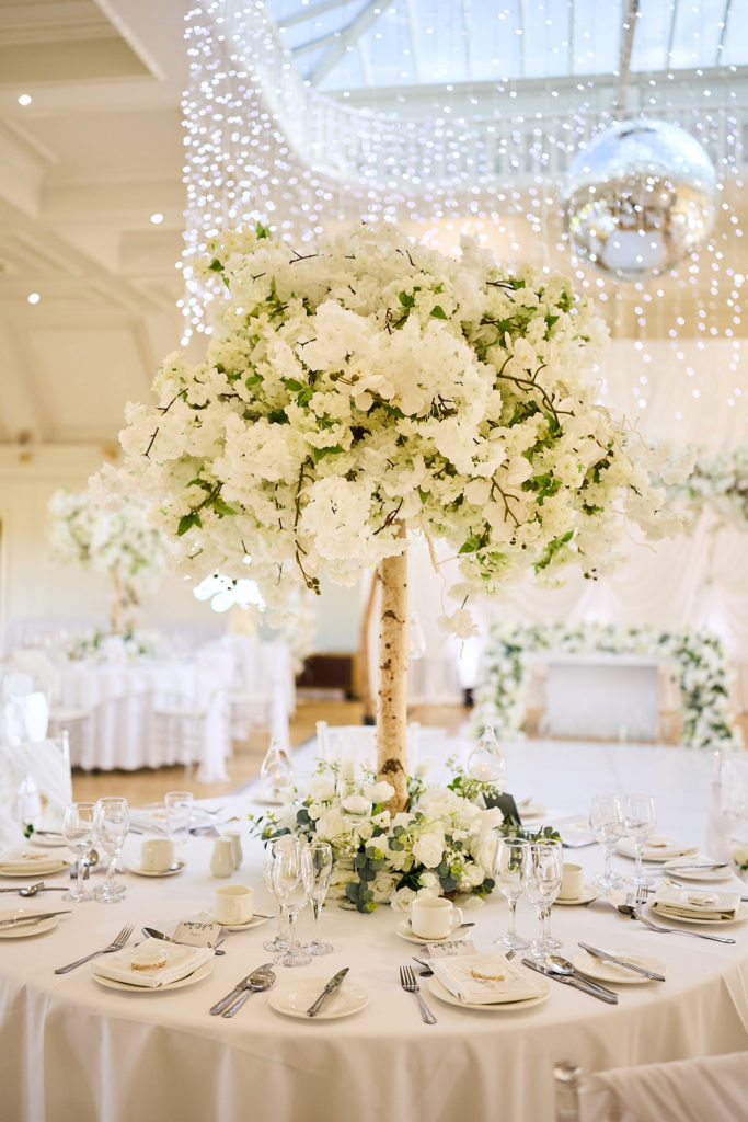 Tall white floral centrepiece on a round table under a mirror ball