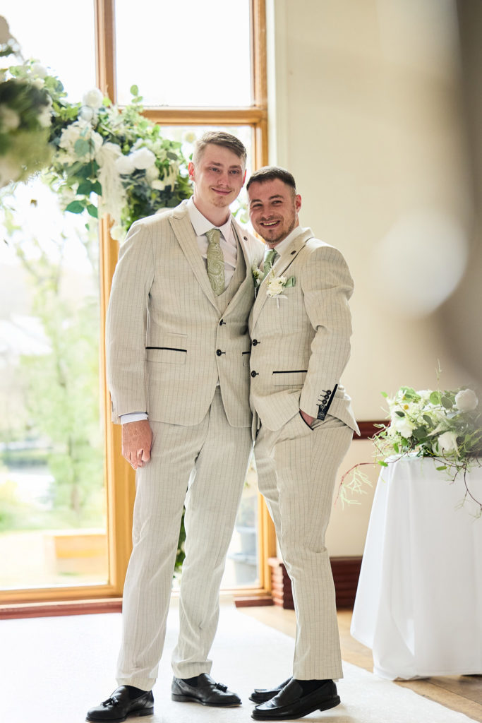 Groom and best man smiling arm in arm in cream suits