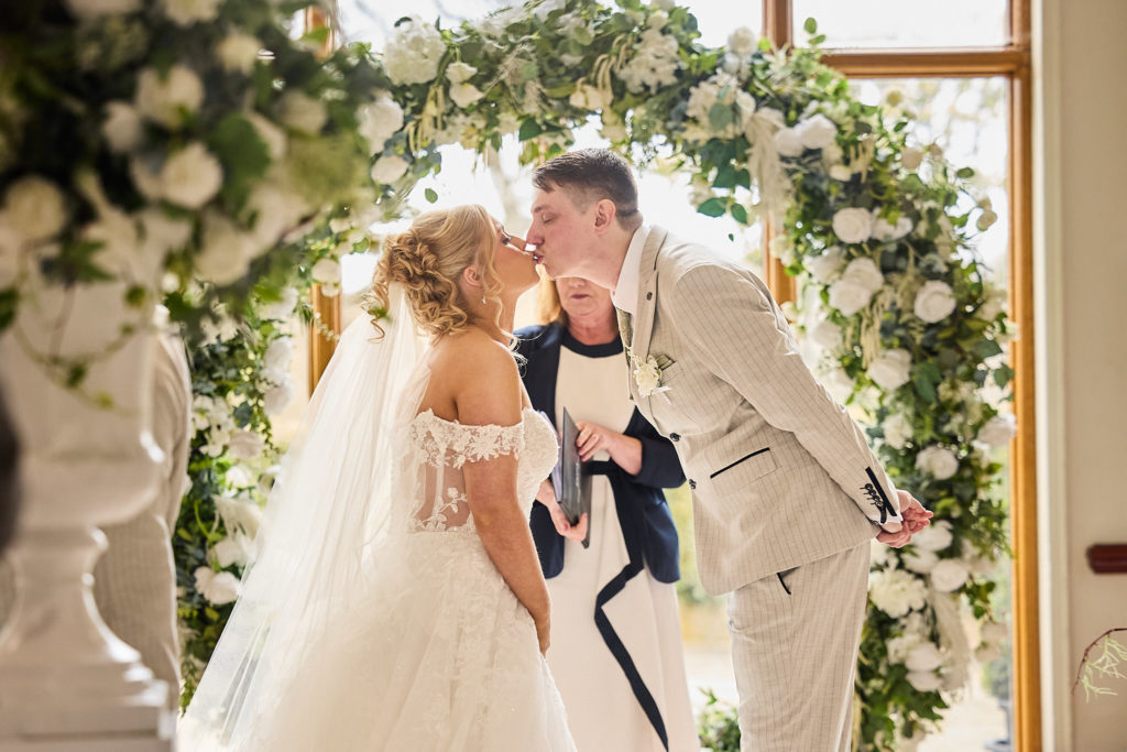 Bride and groom kissing in front of a circular floral arch at Stock Brook Manor
