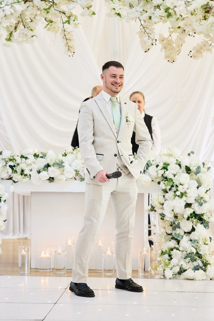 Groom in a cream suit waiting at the front of the ceremony room