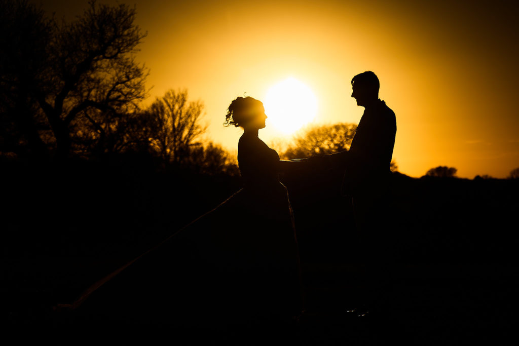 Bride and groom in silhouette against the setting sun at Stock Brook Manor
