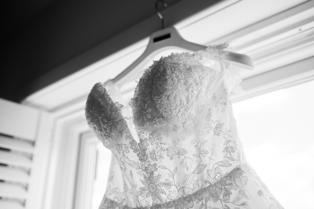 Black and white photo of the lace bodice of the wedding dress hanging at a window