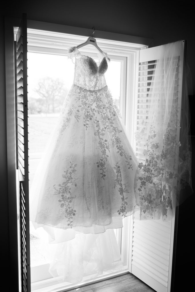 Black and white photo of the wedding dress hanging in a shuttered window