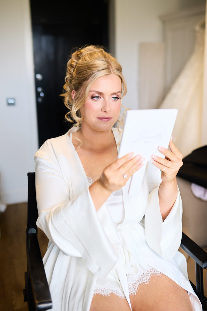 Bride in a white robe reading a card on the wedding morning