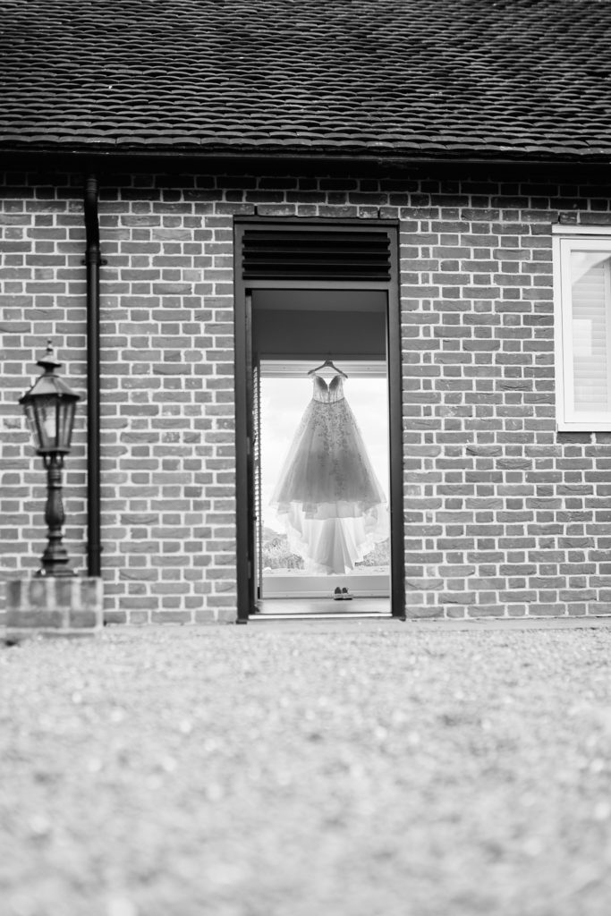 Black and white photo of the wedding dress hanging in the doorway of a brick building