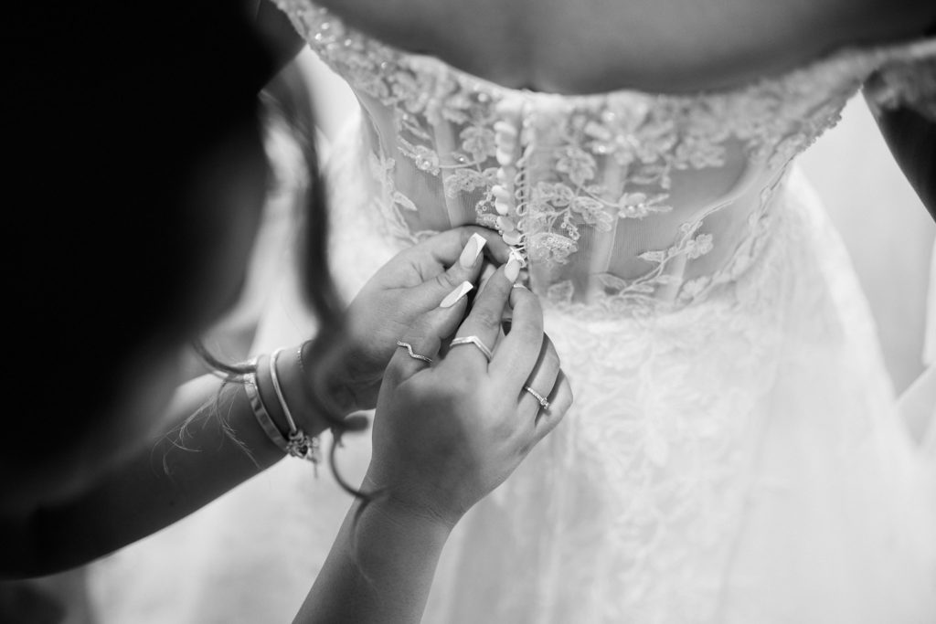 Black and white close-up of the buttons being fastened on the back of the wedding dress