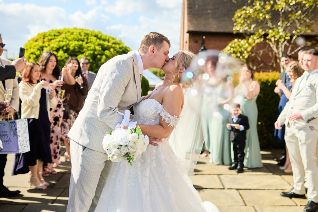 Bride and groom kissing outside as their guests look on