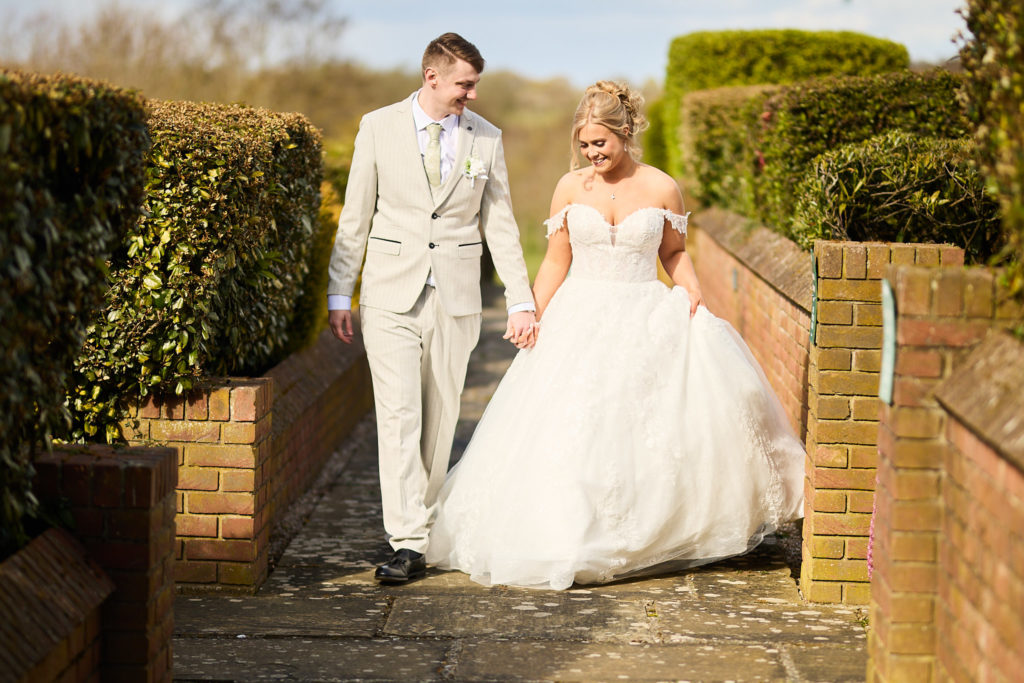 Bride and groom walking hand in hand between the hedges at Stock Brook Manor