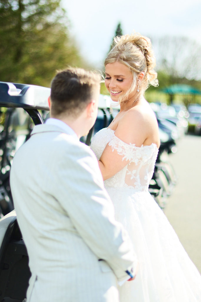 Bride smiling at the groom beside the golf buggies at Stock Brook Manor
