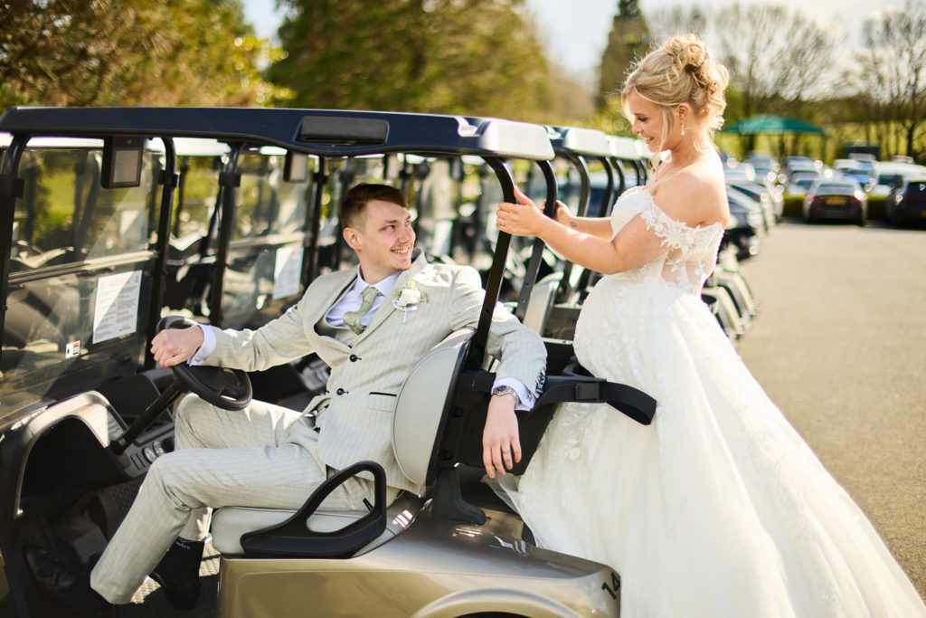 Groom at the wheel of a golf buggy with the bride standing beside him at Stock Brook Manor