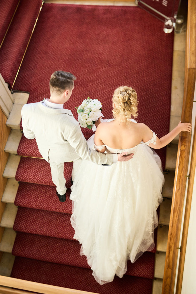Bride and groom walking down a red-carpeted staircase, seen from above