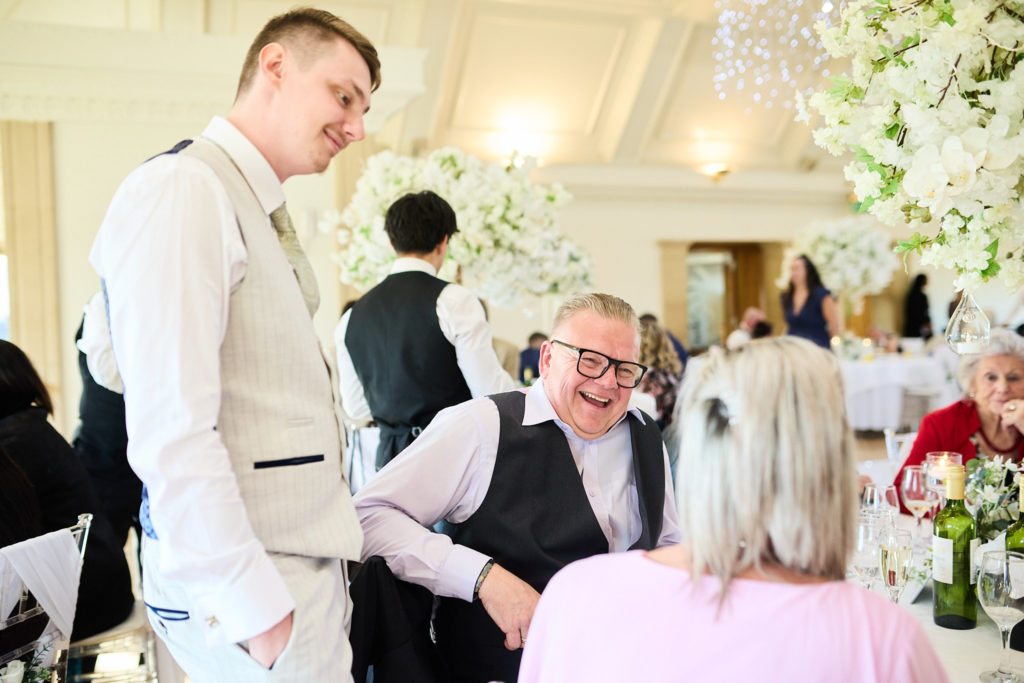 Groom laughing with seated guests at the reception