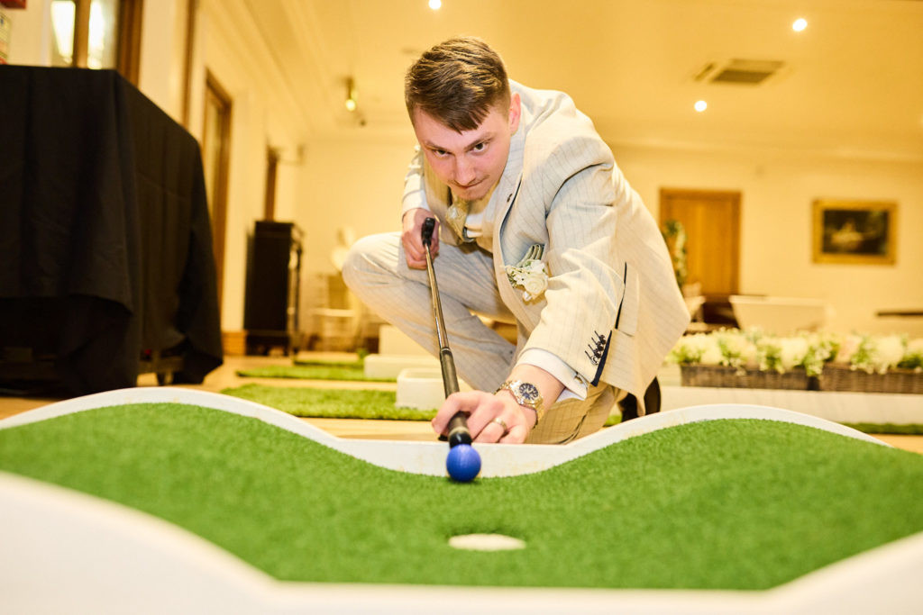 Groom lining up a putt on an indoor mini golf game at his golf themed wedding