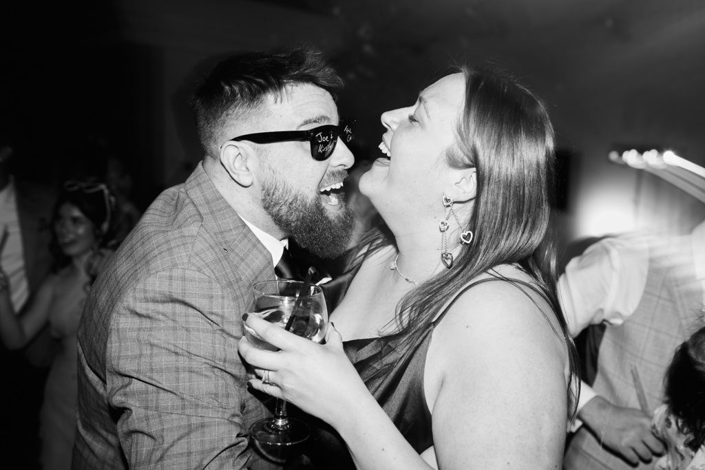 Black and white photo of a guest in sunglasses dancing with a laughing woman