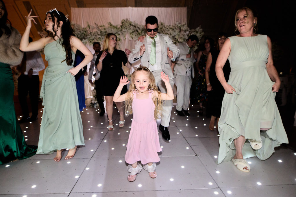 Flower girl in a pink dress dancing with bridesmaids in sage green