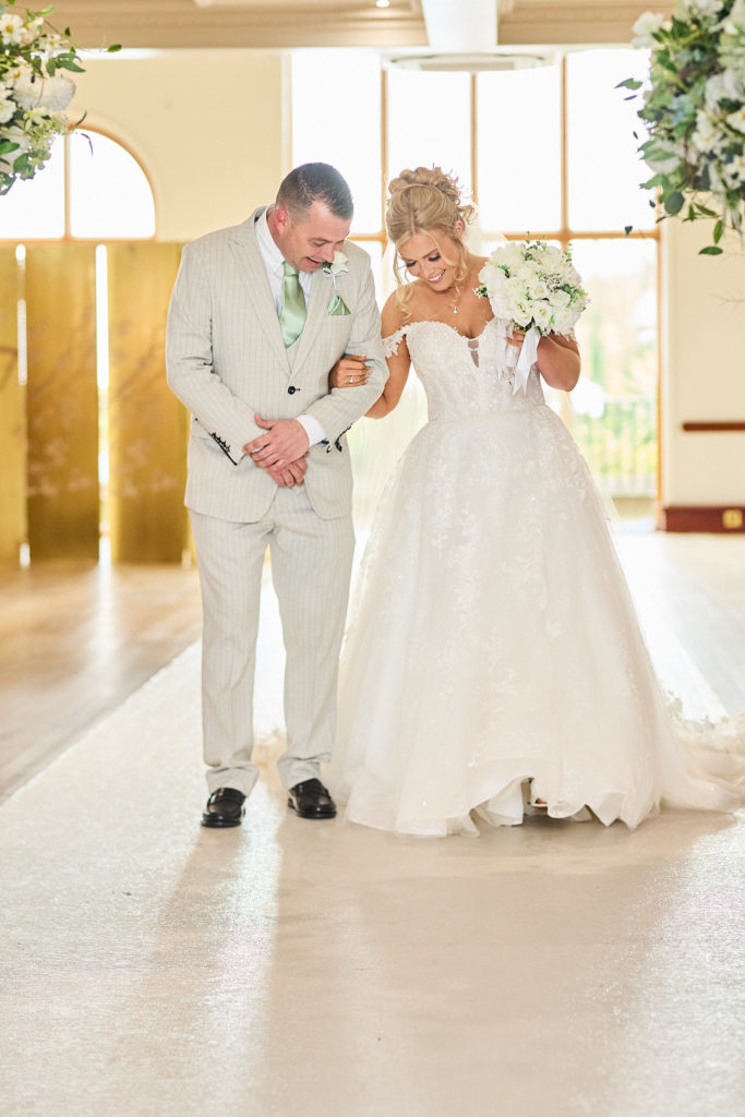 Bride arm in arm with a man in a cream suit on the way to the ceremony
