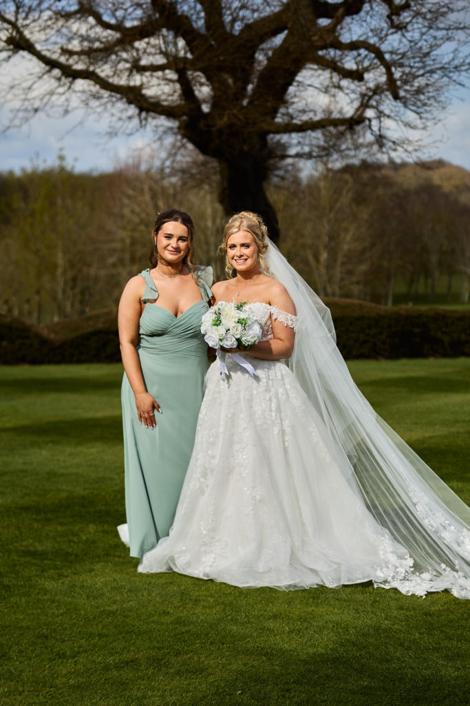 Bride with a bridesmaid in a sage green dress on the lawn at Stock Brook Manor