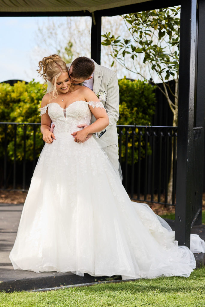 Groom kissing the bride's neck from behind in the bandstand at Stock Brook Manor