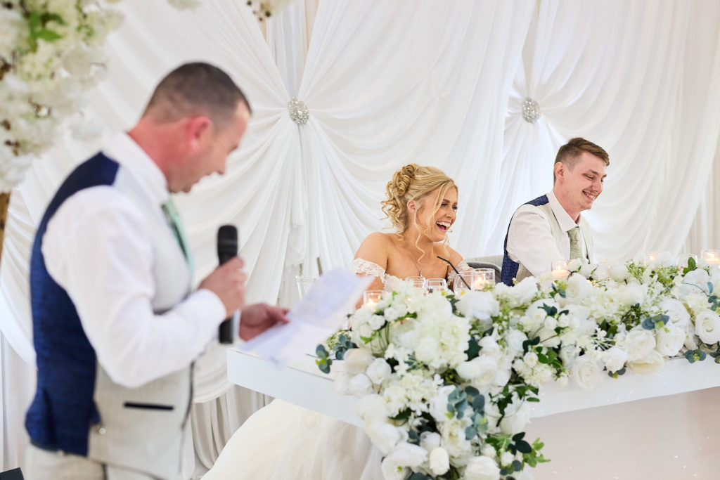 Man in a waistcoat giving a speech as the bride laughs