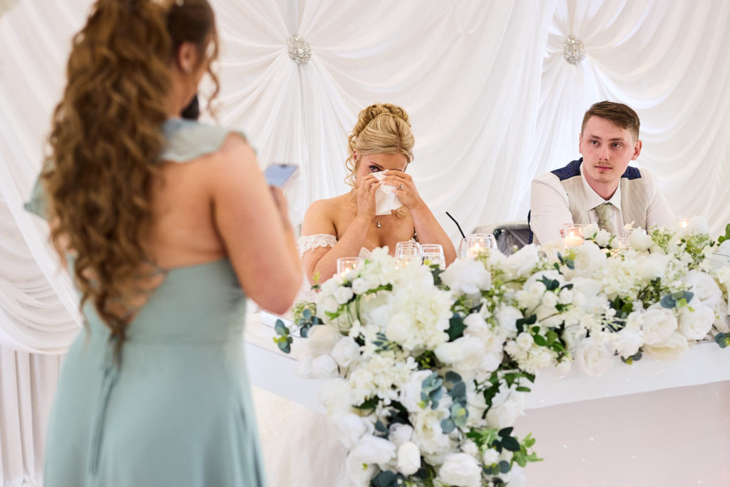 Bride wiping away a tear as a bridesmaid gives her speech