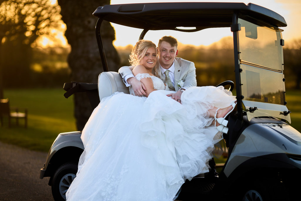 Bride and groom laughing in a golf buggy at sunset at Stock Brook Manor