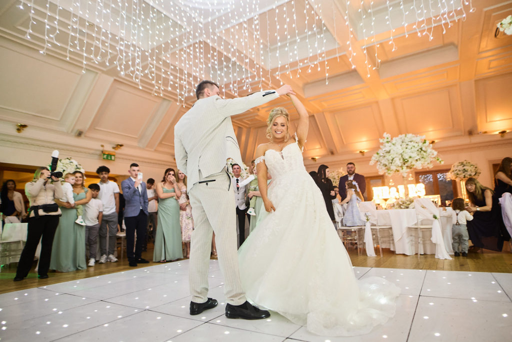 Groom twirling the bride during their first dance under fairy lights
