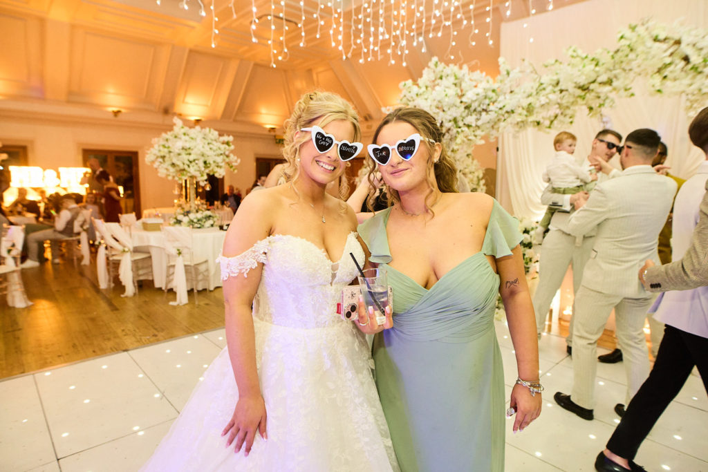 Bride and bridesmaid in heart-shaped sunglasses at the evening reception