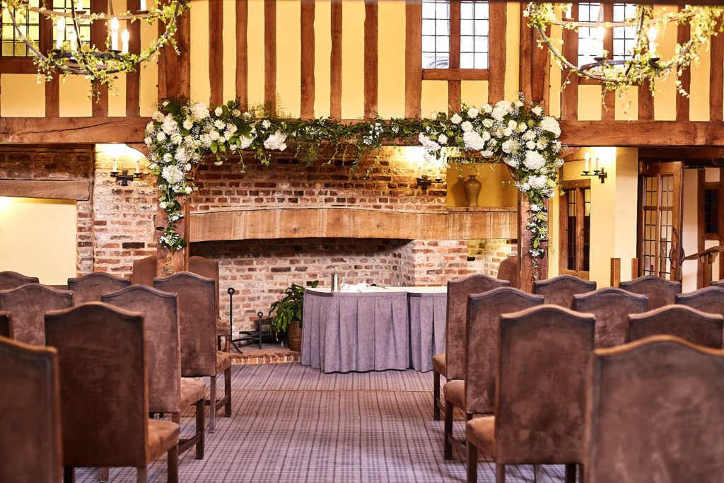 Fireplace dressed with a garland of white flowers in the ceremony room at The Swan at Lavenham