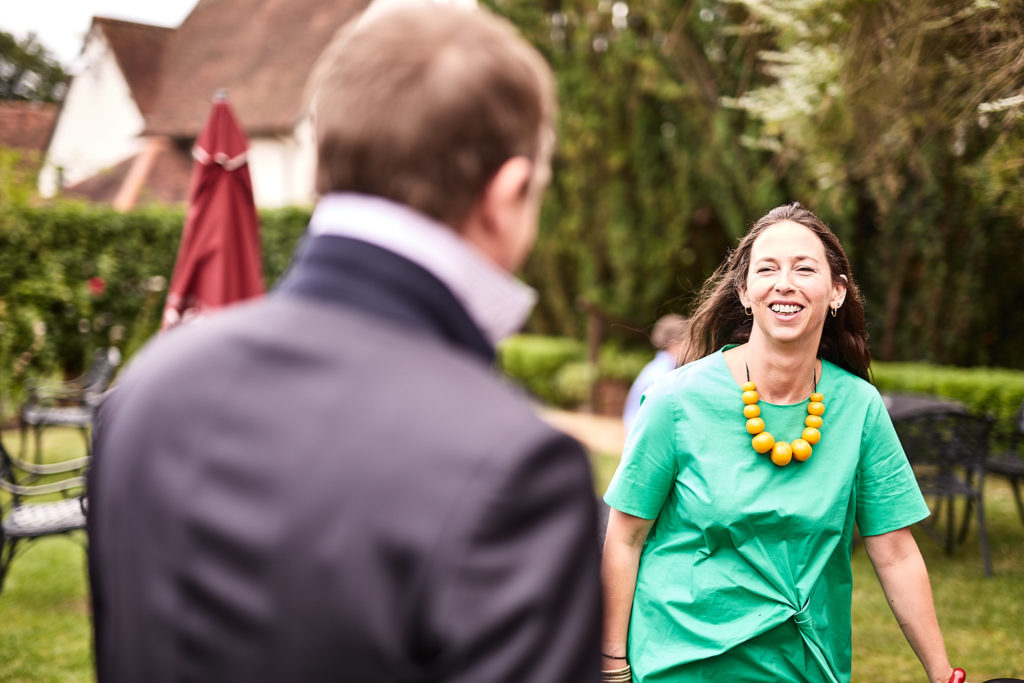 Wedding guest in a green dress laughing as she walks across the garden