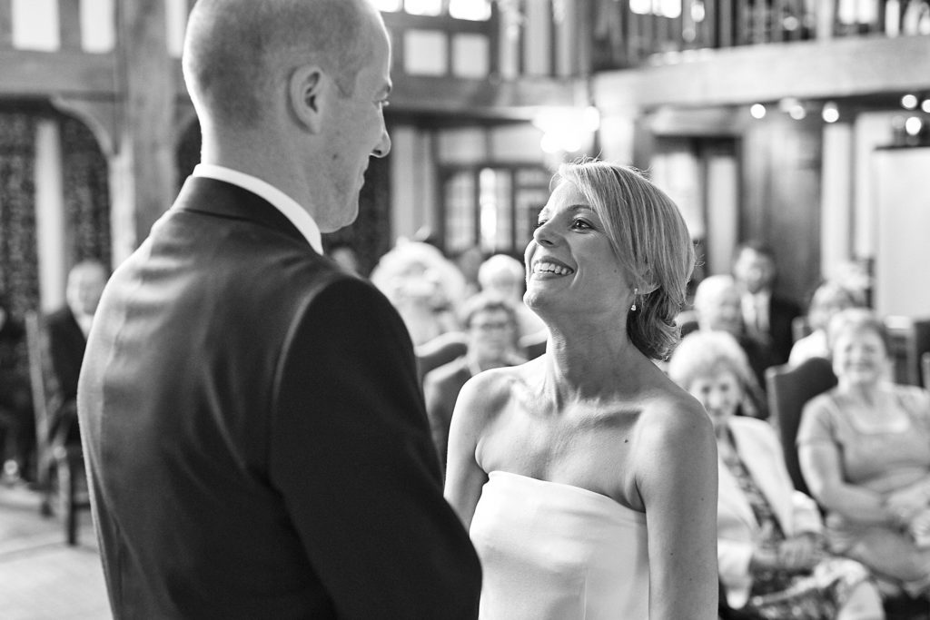 Black and white photo of the bride smiling up at the groom during the ceremony