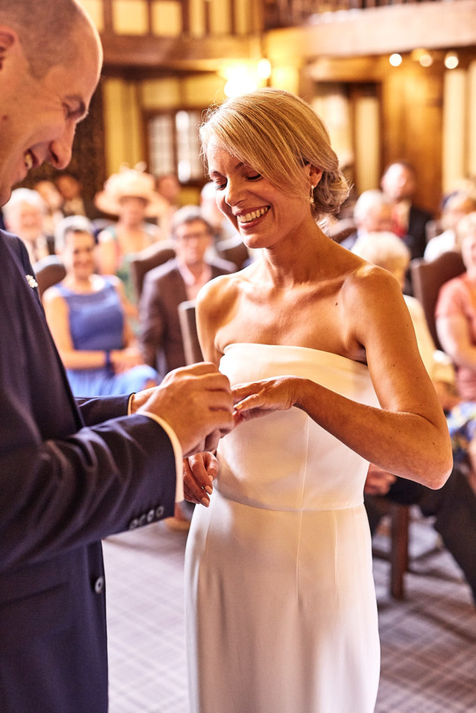 Bride smiling as the groom places the ring on her finger
