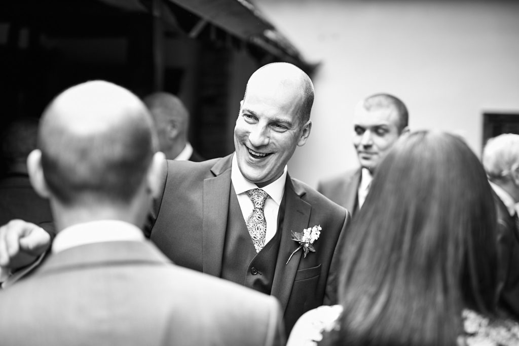 Black and white photo of the groom laughing with guests