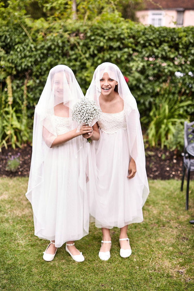 Two flower girls in white dresses giggling under their veils