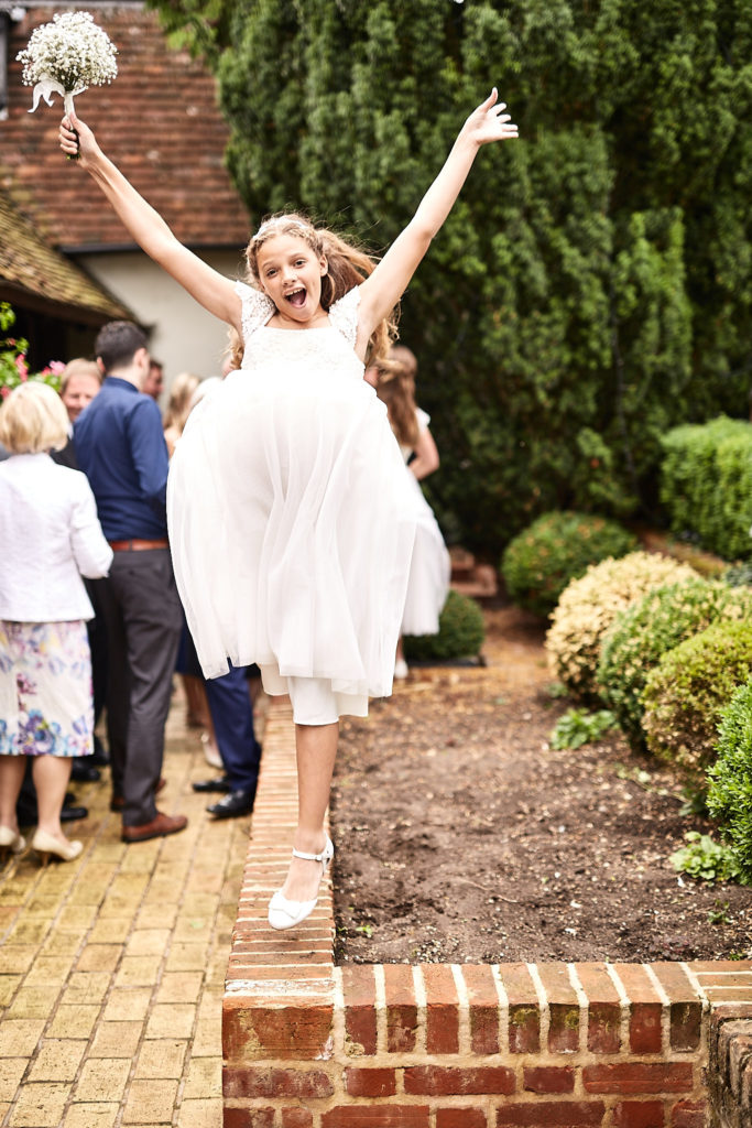 Flower girl jumping off a brick wall with her arms in the air