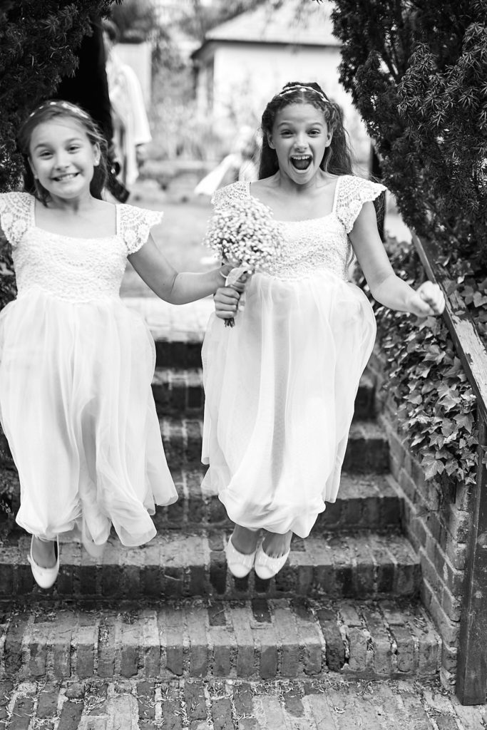 Black and white photo of two flower girls jumping down the garden steps