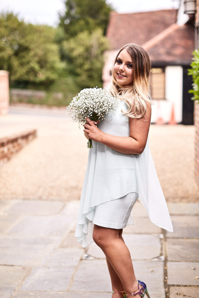 Bridesmaid in a white dress holding a gypsophila posy outside The Swan at Lavenham