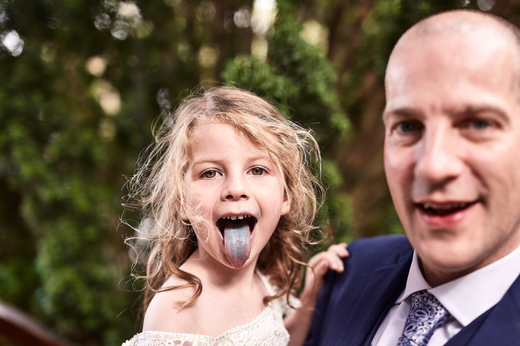 Flower girl sticking out a blue tongue as a man pulls a face beside her