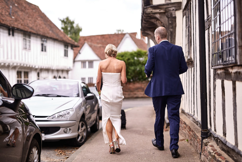Bride and groom walking through the timber-framed streets of Lavenham, seen from behind