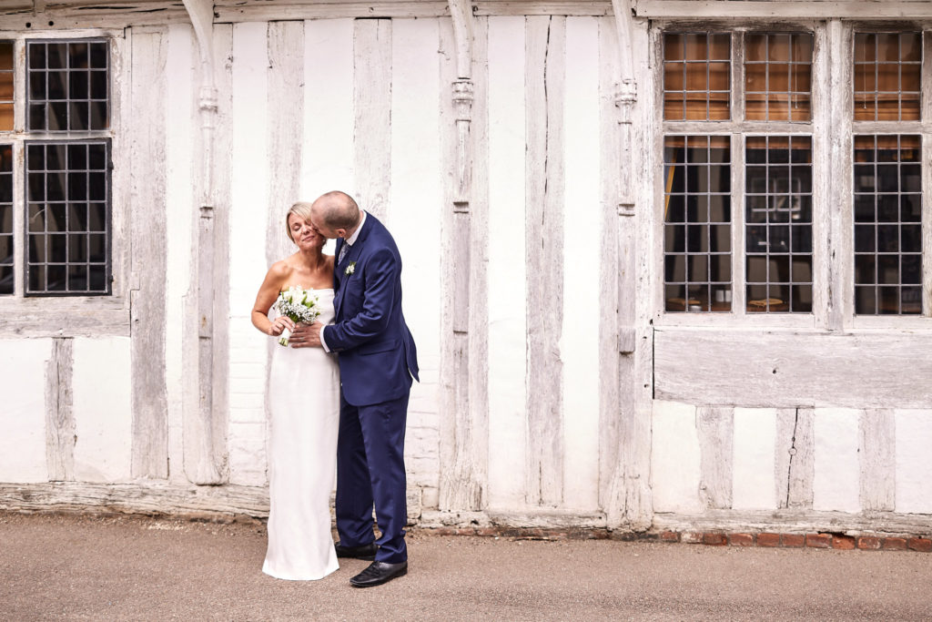 Bride and groom kissing in front of a white timber-framed building in Lavenham