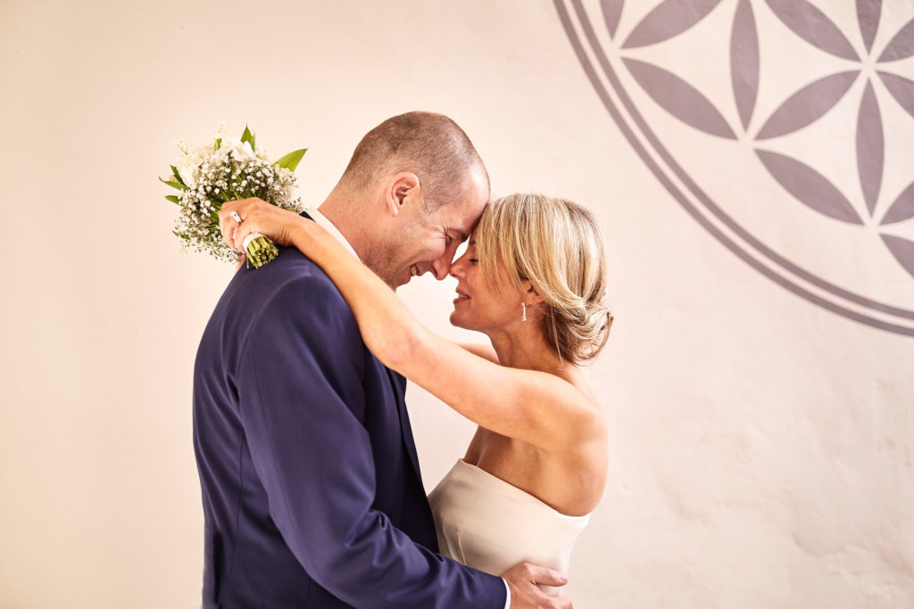 Bride and groom forehead to forehead with her arms round his neck, Lavenham, Suffolk