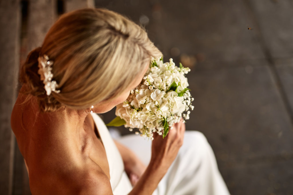 Back of the bride's updo with pearl hairpins as she lifts her bouquet