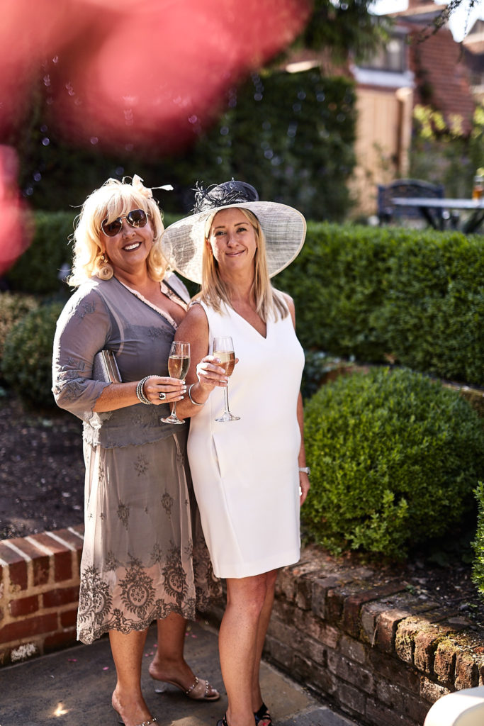 Two wedding guests with drinks in the garden, one in a wide-brimmed hat