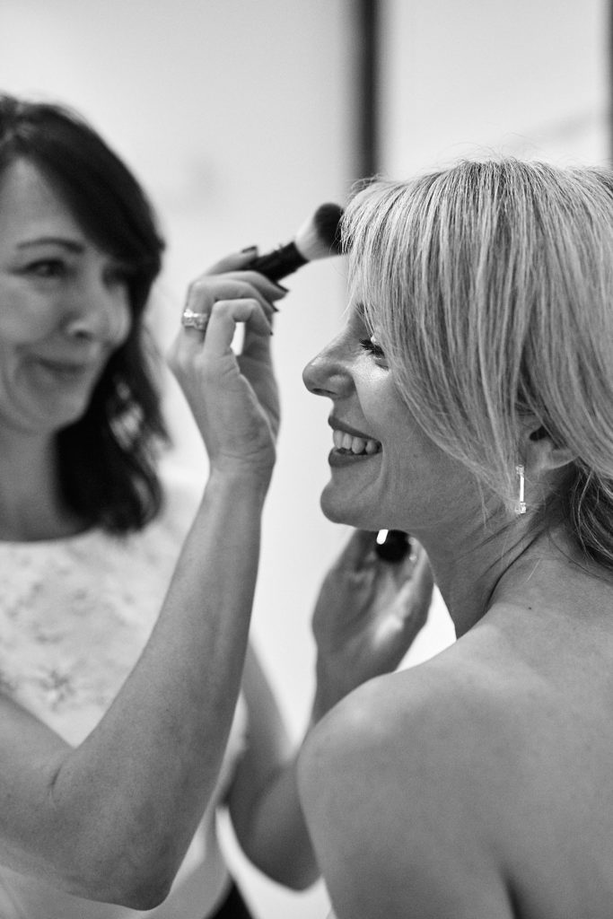 Black and white photo of the bride laughing as her make-up is applied