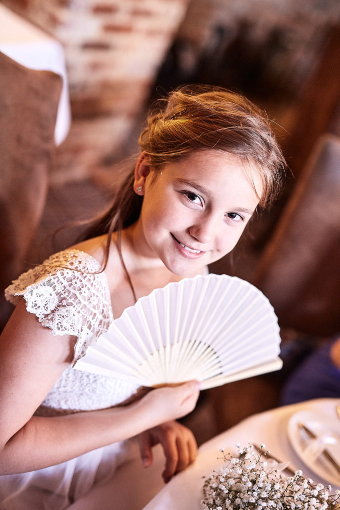 Flower girl holding a white paper fan at the table