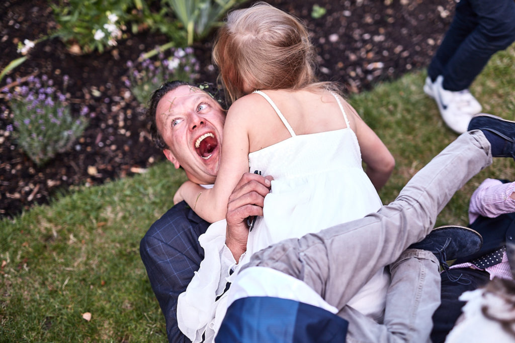 Man laughing on the grass as children climb all over him